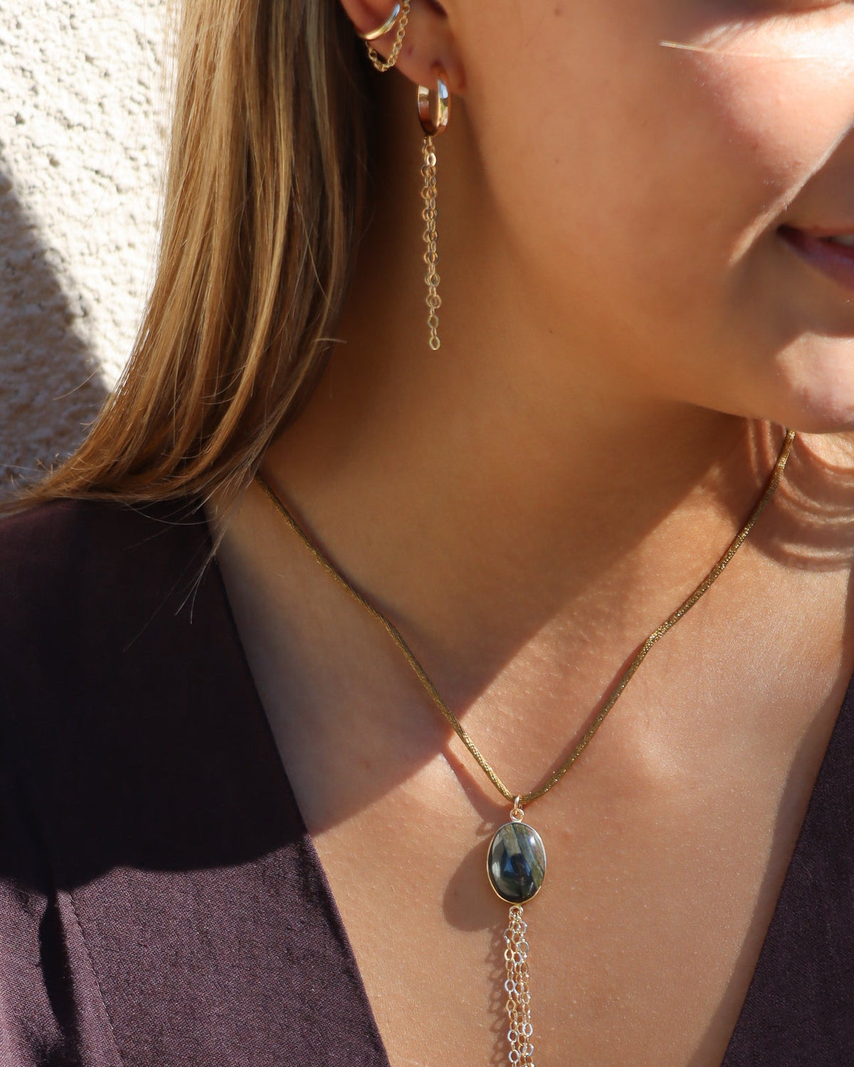 Close-up of a layered necklace featuring an oval dark gemstone pendant with cascading chain fringe, styled with a deep plum top.