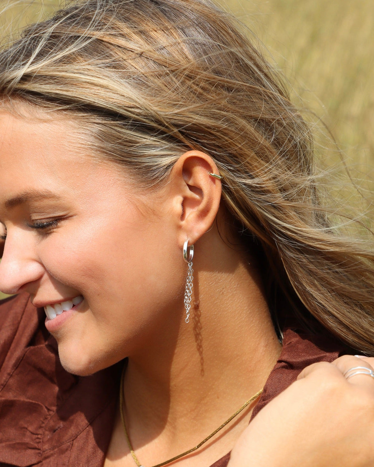 Delicate sterling silver hoop earrings with cascading chain fringe, designed to catch the light with every movement on a model outdoors with other sterling silver jewelry.