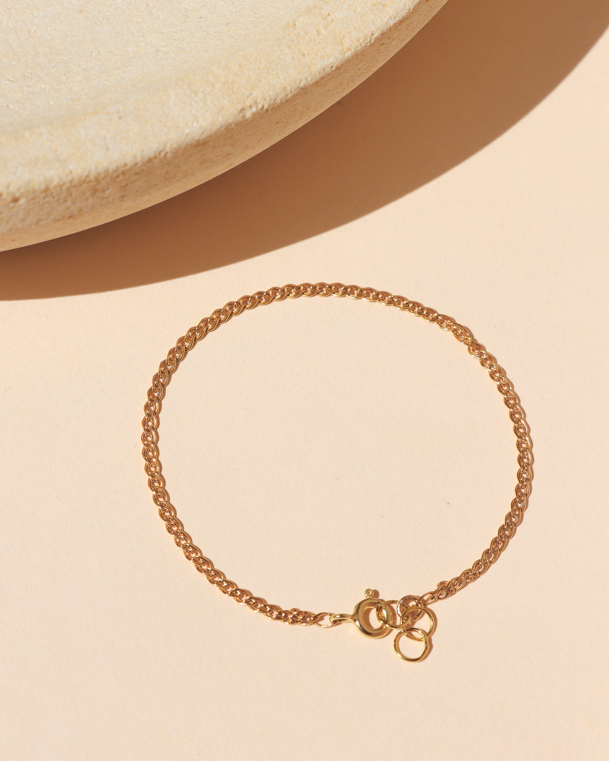 Gold-filled woven chain bracelet with a spring ring clasp, displayed on a neutral surface in warm sunlight.