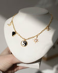 14k gold fill chain with various gold charms, featuring a Butterfly, black heart, yin yang symbol, opal star, and a fleur de lis, photographed on a white bust