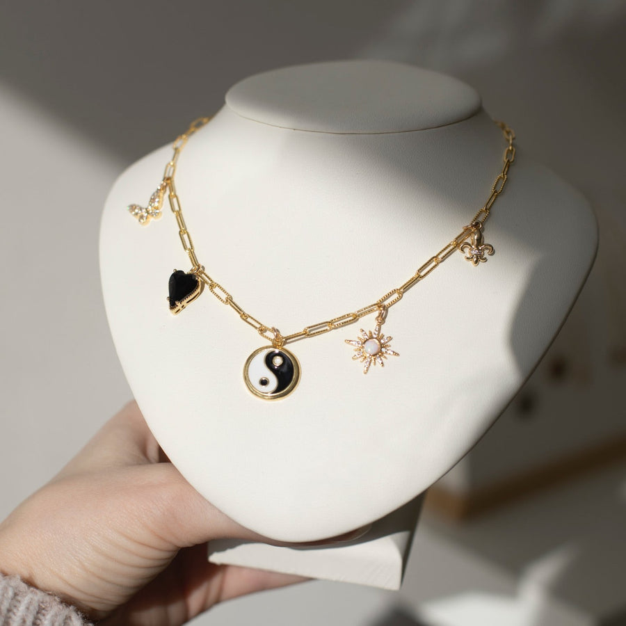 14k gold fill chain with various gold charms, featuring a Butterfly, black heart, yin yang symbol, opal star, and a fleur de lis, photographed on a white bust