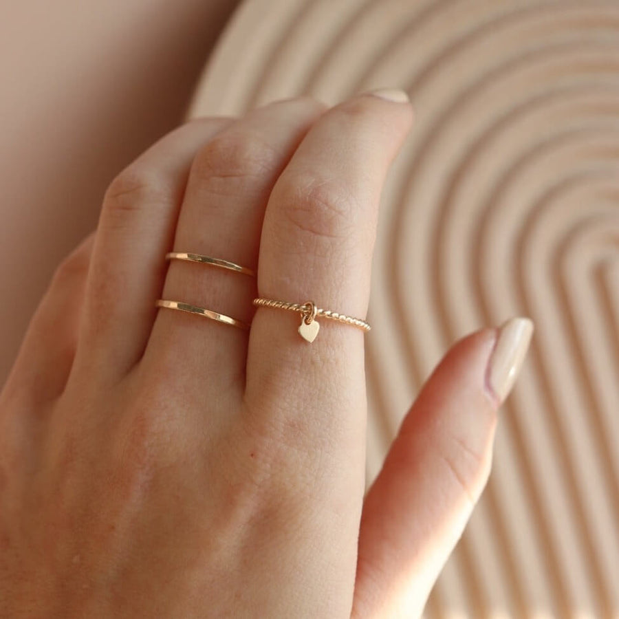 hand wearing a 14k gold fill spiral band with a small heart charm, and a hammered Infinity Ring with two bands