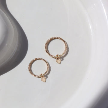 Two 14k gold fill spiral bands with tiny heart charms on each, sizes for an adult and child, photographed on a white dish