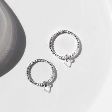 Two 925 sterling silver spiral bands with tiny heart charms on each, sizes for an adult and child, photographed on a white dish
