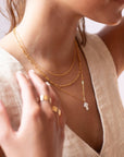 a mother of pearl white cross pendant on a 14k gold fill chain, photographed on a model wearing a cream linen vest and other 14k gold fill chain necklaces made by Token Jewelry