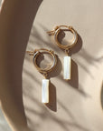 14k gold fill Mother of Pearl Hoops laid on a peach plate in the sunlight. These earring feature a classic hoop with a mother of pearl drop down stone. 
