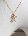 14k gold fill Initial Script Necklace placed on a white pot in the sunlight.