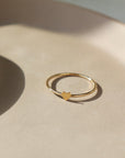 14k gold fill Tiny heart ring laid on a tan plate in the sunlight. This ring features a smooth band with a tiny heart. This ring is so cute stacked with any of the stacking rings at Token Jewelry. 