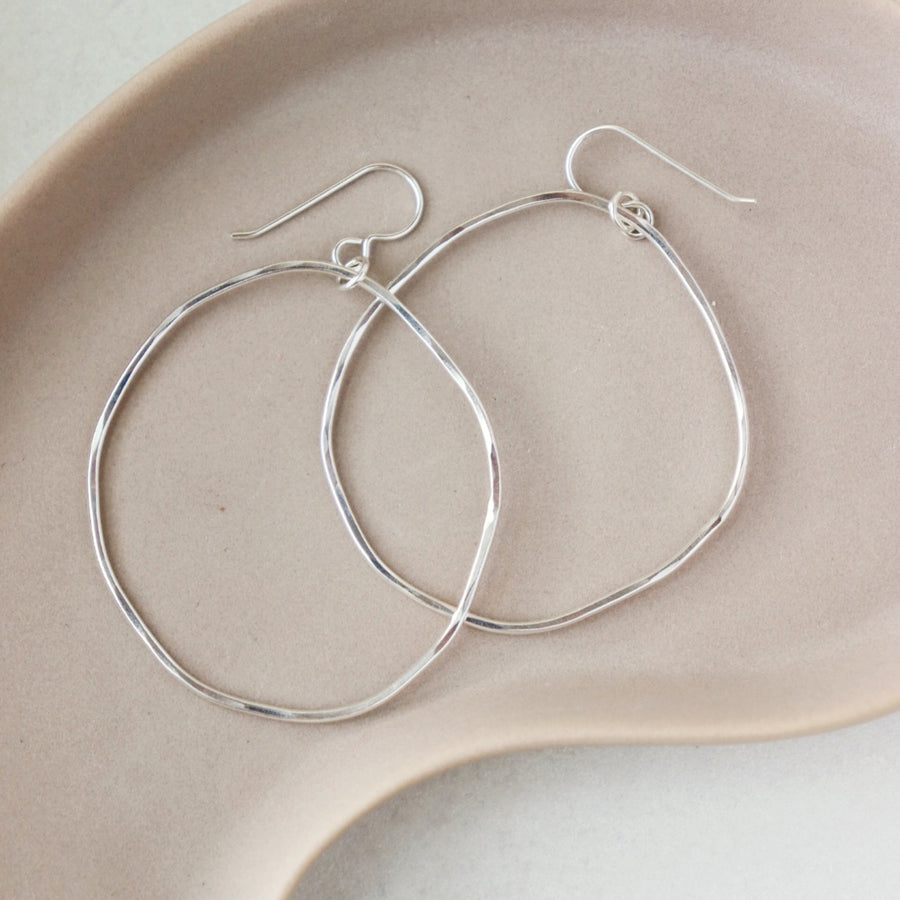 925 sterling silver form hoops placed on a peach plate set in the sunlight. These earring feature a large hoop that is hammered on both sides and has a hook for a earring