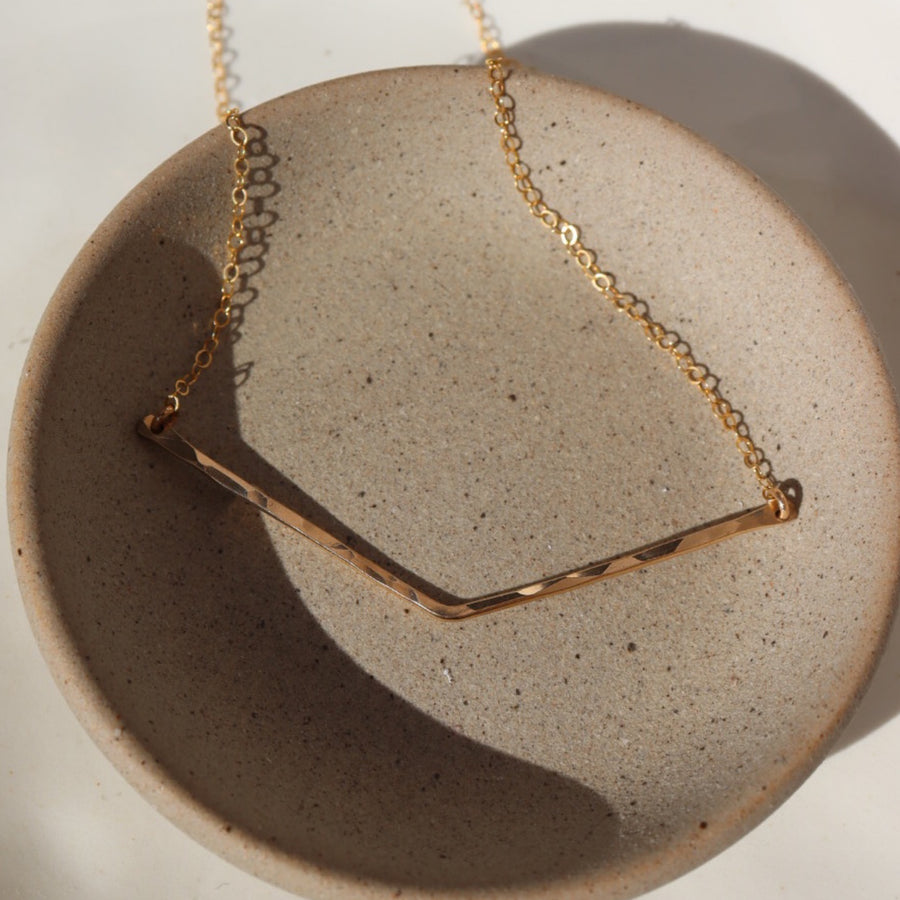 14k gold fill Archer necklace laid across a gray plate. Handmade is Eau Claire, WI.