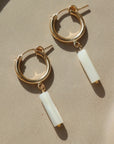 14k gold fill Mother of Pearl Hoops laid on a peach plate in the sunlight. These earring feature a classic hoop with a mother of pearl drop down stone.