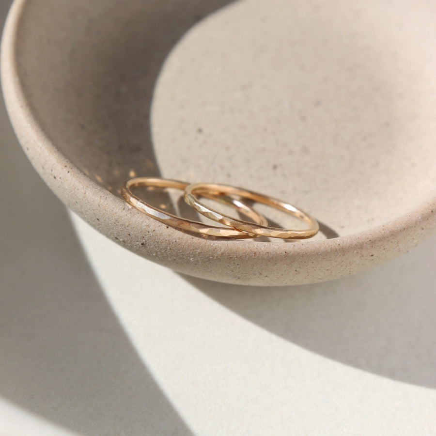 14k gold fill hammered standing ring is placed on top of each other. The rings then are placed on a gray plate laying in the sunlight. These rings are lightly hammered gold stacking ring, handmade by Token Jewelry in Eau Claire, Wisconsin