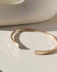 14k gold fill Halo Cuff placed on a white plate sitting in the sunlight.