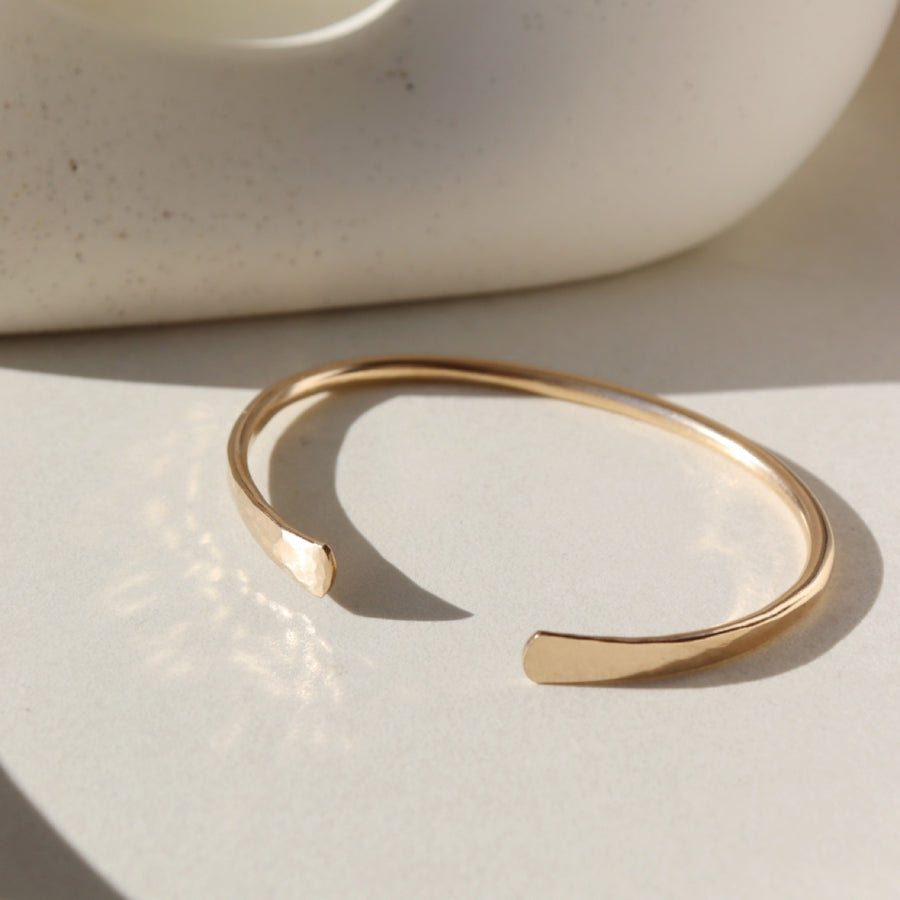 14k gold fill Halo Cuff placed on a white plate sitting in the sunlight.