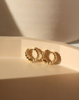 14k gold fill Croissant Huggie Hoops placed on a peach colored plate sitting in the sunlight.