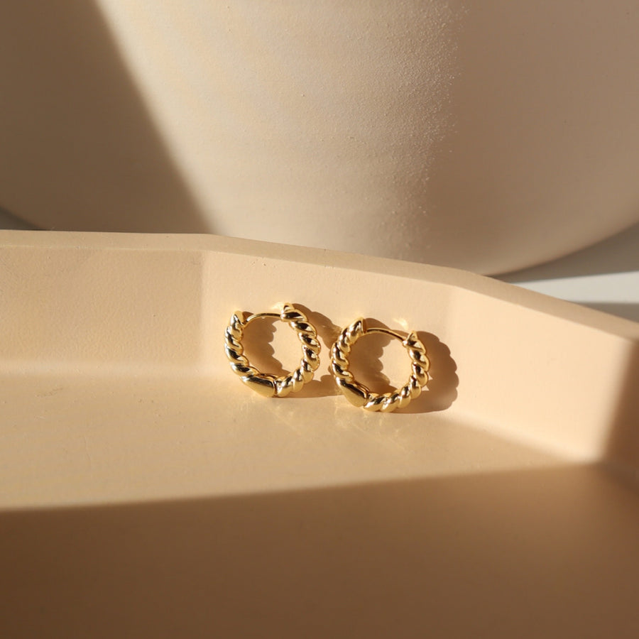 14k gold fill Croissant Huggie Hoops placed on a peach colored plate sitting in the sunlight.