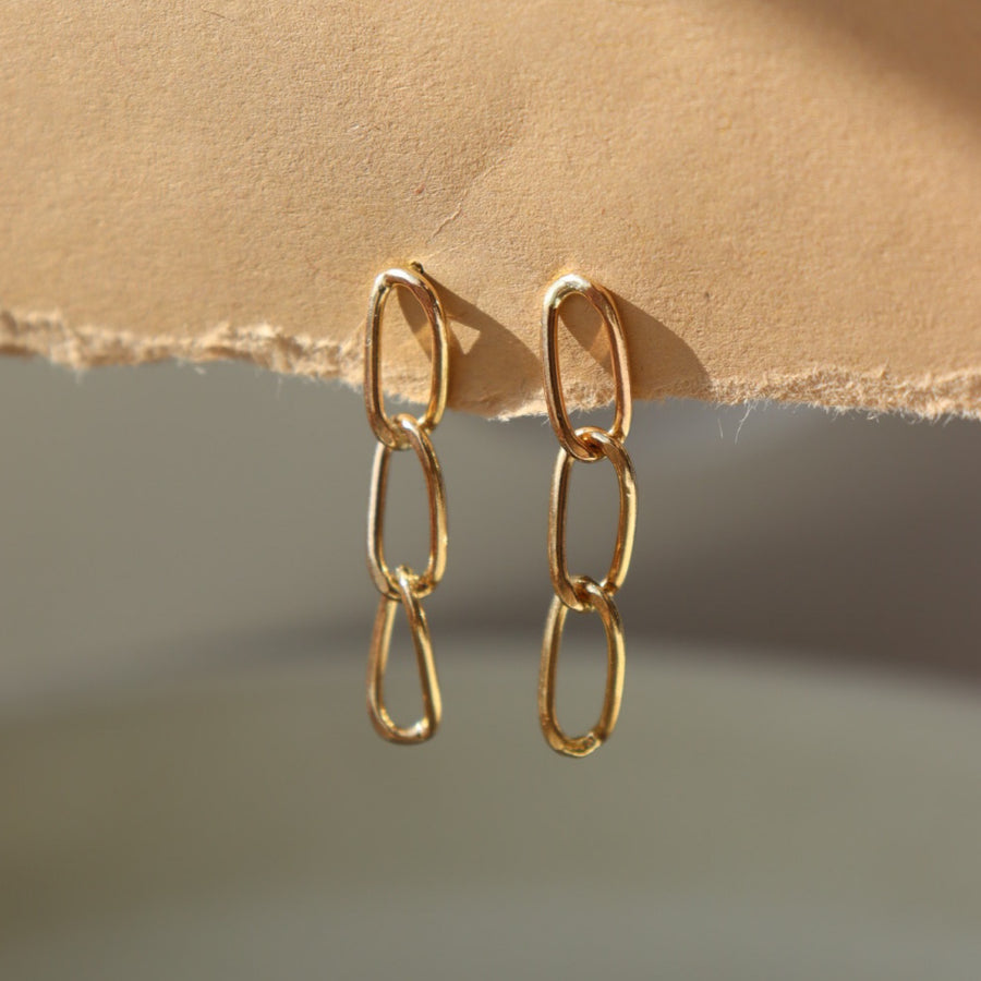 14k gold fill curve studs hanging from a brown paper sheet. Handmade in Eau Claire Wisconsin.