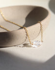 a clear double terminated quartz gemstone, known as a Herkimer Diamond, hangs from a delicate gold filled oval cable chain and is displayed on a ceramic jewelry dish