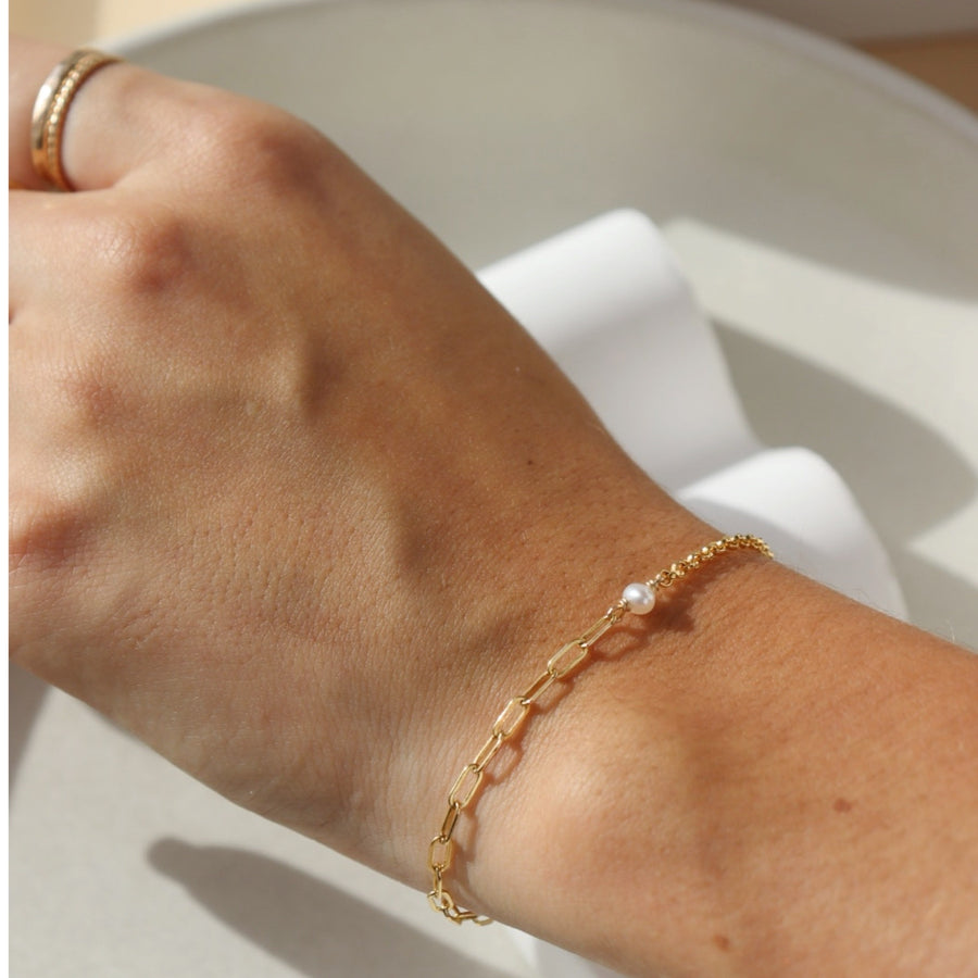 Model wearing the Emma Bracelet in 14k gold fill the bracelet  featuring the narrow link chain, a tiny pearl gemstone, and the Dylan chain. The jewelry is handmade in Eau Claire Wisconsin, at Token Jewelry.