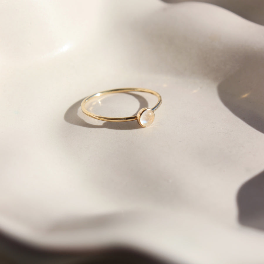 14k gold fill moonstone ring 4mm set on a white plate. This ring features a simple band with a moonstone gemstone bezeled to it.
