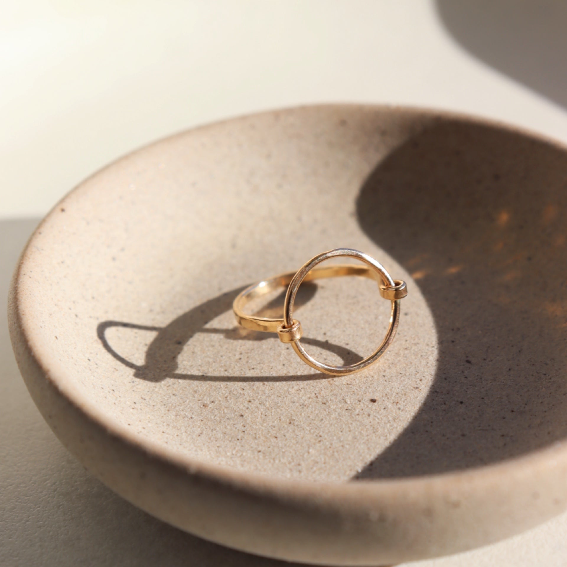 14k gold fill Eternity Ring is sitting on gray plate set in the sunlight.  This ring is features a circle disc that is wrapped with an additional wire as the band. The band is hammered on the disc as well as the band. The jewelry is hypoallergenic and nickel free. Handmade in Eau Claire, Wisconsin.