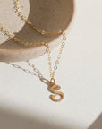 14k gold fill initial Script Necklace laid on a gray plate in the sunlight. 