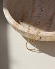 14k gold fill Eternity Necklace placed on a cream colored dish. This necklace and plate is sitting in the sunlight. This necklace features an open circle disc that is attached to our simple chain. Token Jewelry is hypoallergenic and nickel free. - Token Jewelry