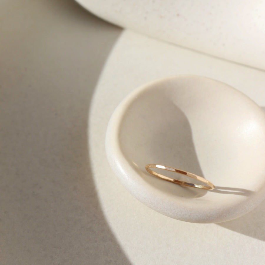 14k gold fill stacking ring laid on white plate in the sunlight. This ring features a simple band with hammering on the outside. 