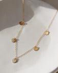 14k gold fill Suncatcher necklace laid on a white plate in the sunlight. This Necklace features the simple chain with 5 circle disc. This necklace is perfect for layering.