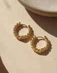 14k gold fill Croissant Huggie Hoops laid on the peach paper.