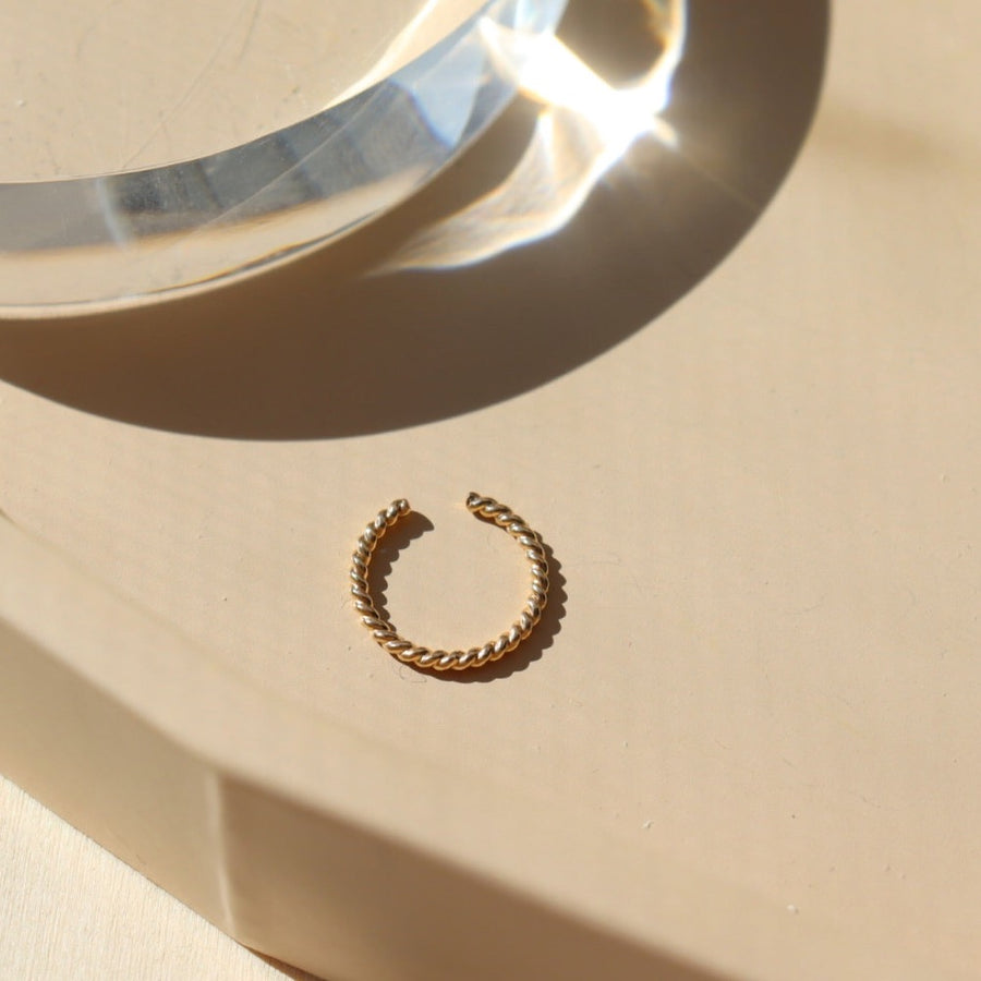 14k gold fill Spiral Ear Cuff laid on a peach plate in the sunlight. This ear cuff features the spiral allusion of a twist of two metals. This ear cuff is easy to wear on your ear.