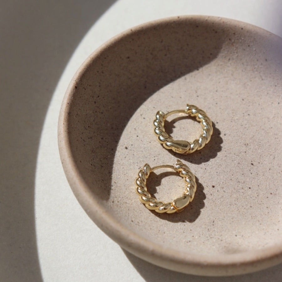 14k gold fill Croissant Huggie Hoops placed on a gray plate sitting in the sunlight. 
