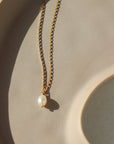 14k gold floating pearl necklace laid on a peach colored plate laying in the sunlight.