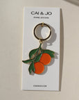 Cai & Jo enamel oranges keychain on a paper backing