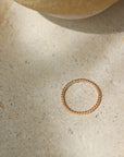 14k gold fill Spiral Midi Ring laid on a tan plate in the sunlight. This ring band features a spiral look and is perfect for stacking.