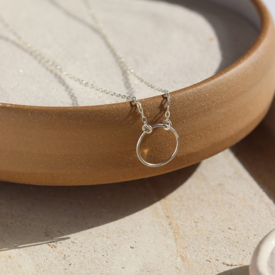 925 Sterling Silver Eternity Necklace placed on a cream colored dish. This necklace and plate is sitting in the sunlight. This necklace features an open circle disc that is attached to our simple chain. Token Jewelry is hypoallergenic and nickel free. - Token Jewelry