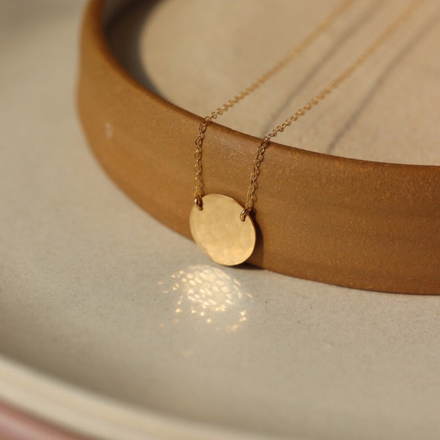hand stamped letters on a tiny disc hanging from a dainty cable chain. handmade personalized necklace in 14k gold fill