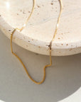14k gold fill Necklace laid on a cream plate in the sunlight.