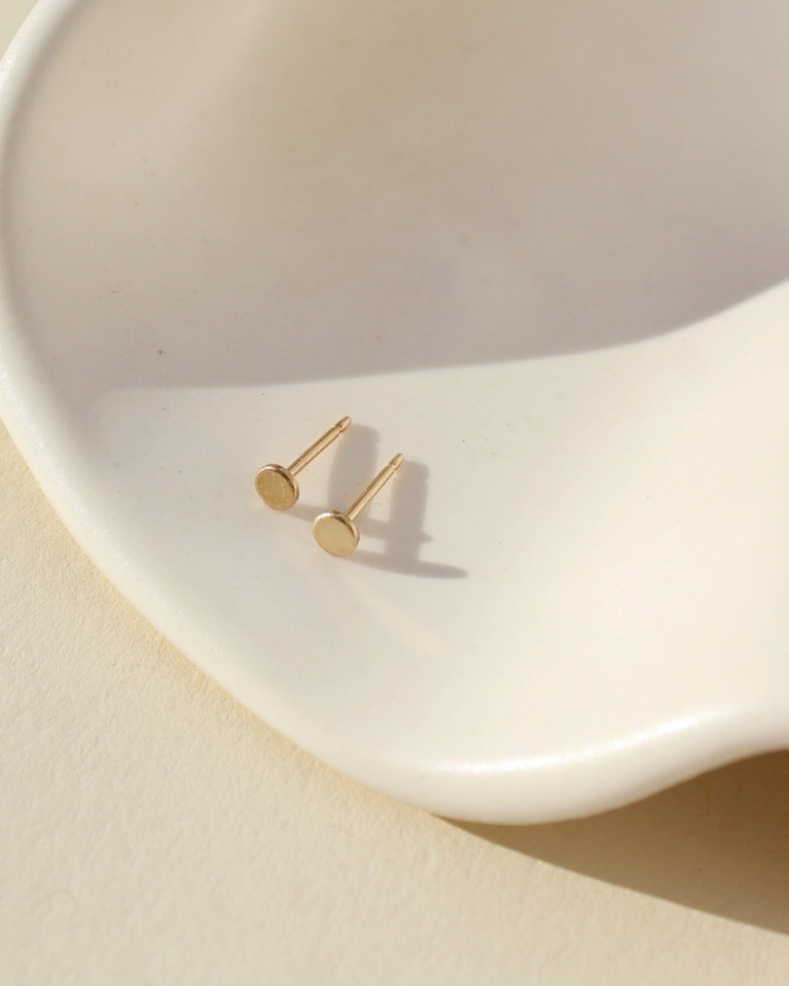 14k gold fill polka dot studs laid on white wavy dish in sunlight
