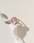 14k gold filled Pippa Ring laid on a white paper in the sunlight. This ring features a sprial band with a pink kunzite gemstone.