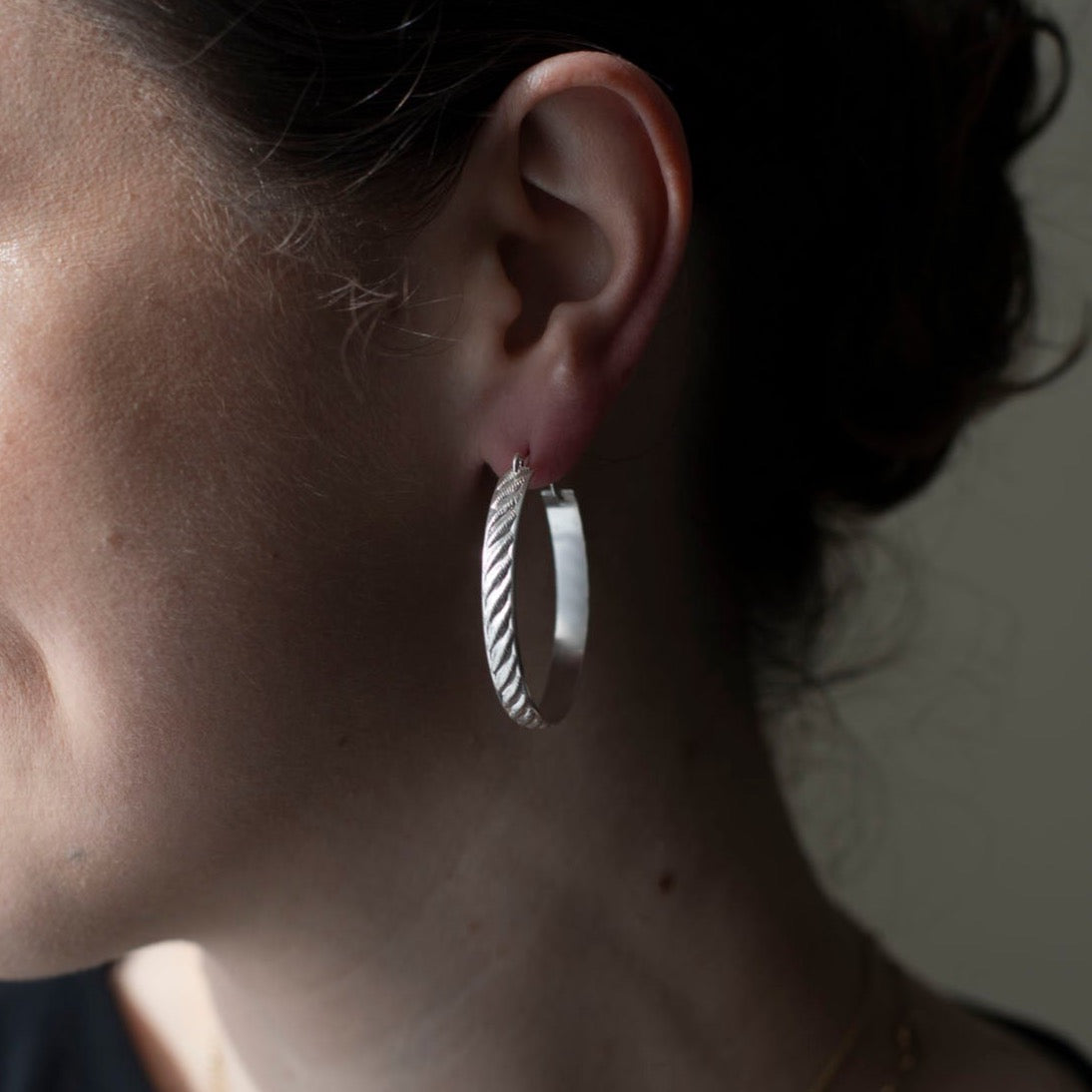 925 sterling silver hoop earrings, approximately 1.5&quot; diameter with a soft ripple pattern engraved. they&#39;re photographed on a brunette model in shadow and sun