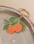 enamel keychain of two oranges hanging below a leaf, on a ceramic plate